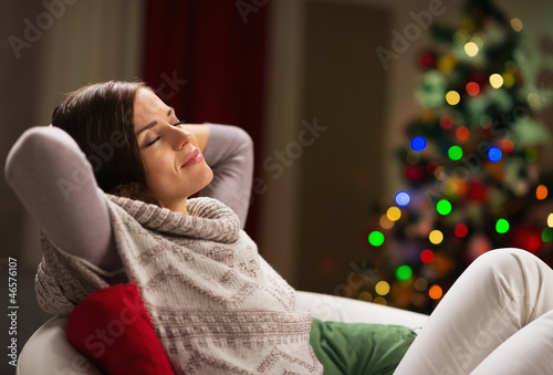 Photo: Young woman relaxing on chair in front of Christmas tree Young woman relaxing on chair in front of Christmas tree