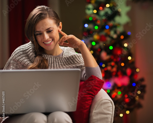 Photo: Happy woman looking in laptop in front of Christmas tree Happy woman looking in laptop in front of Christmas tree