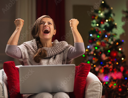 Photo: Woman with laptop rejoicing success in front of Christmas tree Woman with laptop rejoicing success in front of Christmas tree