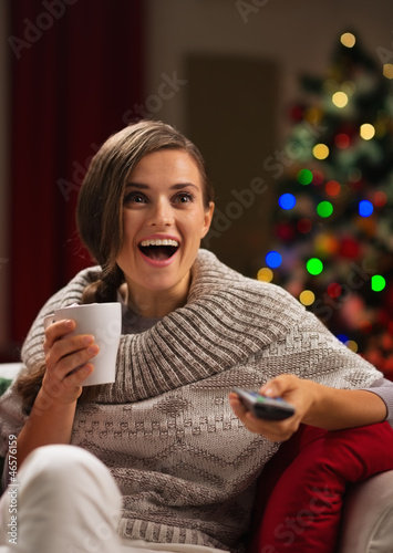 Photo: Surprised young woman with cup of hot beverage looking TV Surprised young woman with cup of hot beverage looking TV