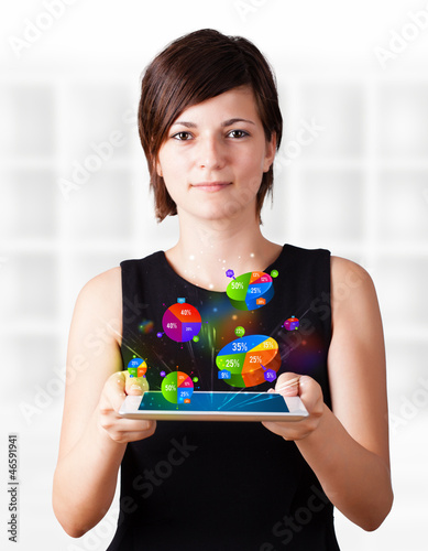 Photo: Young woman looking at modern tablet with pie charts Young woman looking at modern tablet with pie charts