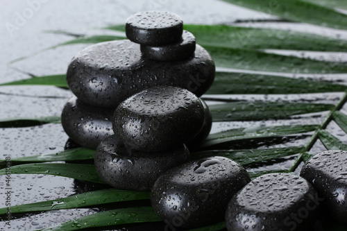 Photo: Spa stones with drops on green palm leaf on grey background Spa stones with drops on green palm leaf on grey background