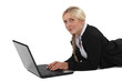 Blond businesswoman laying on front and typing on laptop