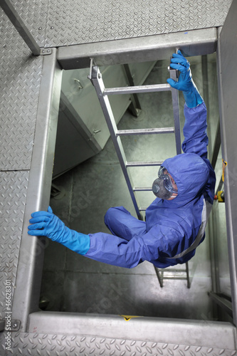 Photo: specialist in protective uniform going up a metal ladder specialist in protective uniform going up a metal ladder