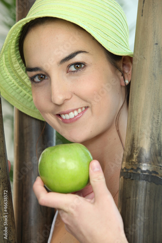 Photo: Woman stood by wooden poles holding a green apple Woman stood by wooden poles holding a green apple