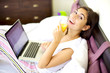 Smiling happy woman working in bed drinking juice