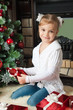 Happy little girl with gifts near christmas tree and fireplace