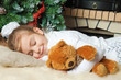Little girl sleeping and hugging her teddy bear near christmas t