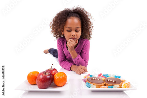 Photo: Little African Asian girl hesiatating between fruits or candy Little African Asian girl hesiatating between fruits or candy