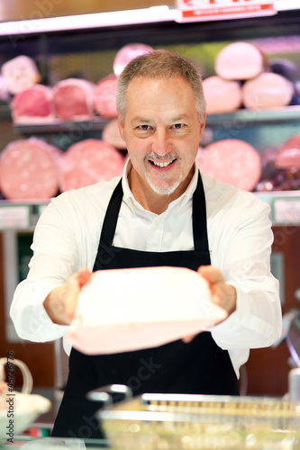 Photo: Smiling butcher giving you a product of his shop Smiling butcher giving you a product of his shop