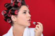 woman with curlers in her hair putting lipstick