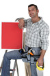 Carpenter with a red sign propped up on his knee