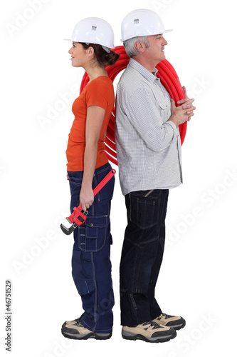 Photo: Experienced plumber stood back to back with young helper Experienced plumber stood back to back with young helper