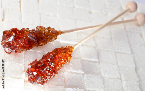 Photo: candy brown sugar on a stick lies on white lumpy sugar.. candy brown sugar on a stick lies on white lumpy sugar..