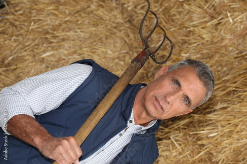 Photo: mature handsome farmer posing with fork against hay background mature handsome farmer posing with fork against hay background