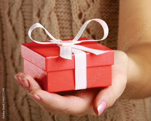 Photo: Female hand holding gift box isolated on red background Female hand holding gift box isolated on red background