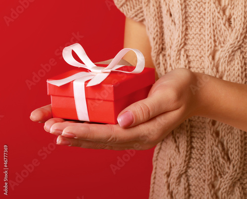 Photo: Female hand holding gift box isolated on red background Female hand holding gift box isolated on red background