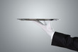 Waiter holding empty silver tray over gray background with copy