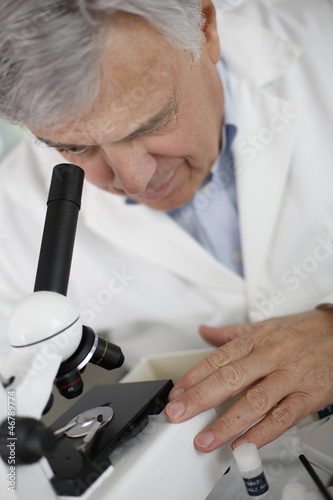 Photo: Scientist in lab looking through microscope lens Scientist in lab looking through microscope lens