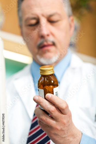 Photo: Mature pharmacist analyzing a product in his store Mature pharmacist analyzing a product in his store