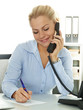 Pretty secretary makes notes while having a call at work
