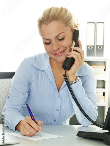 Photo: Pretty secretary makes notes while having a call at work Pretty secretary makes notes while having a call at work