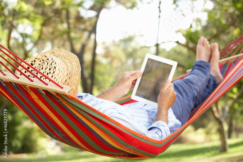 Photo: Senior Man Relaxing In Hammock With E-Book Senior Man Relaxing In Hammock With E-Book