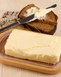 Butter on wooden holder and bread on wooden table close-up