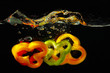 Slices of fresh red, green and yellow pepper falling into water