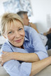 Senior woman sitting in couch, husband in background