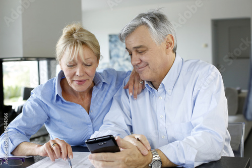 Photo: Senior couple calculting bills amount using smartphone Senior couple calculting bills amount using smartphone