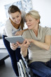 Girl showing tablet to elderly woman in wheelchair