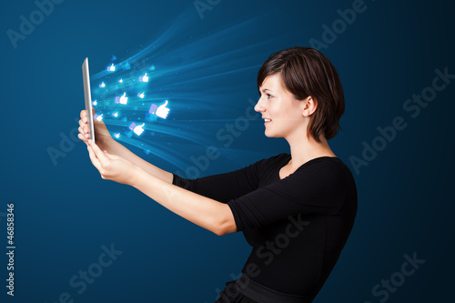 Photo: Young woman looking at modern tablet with abstract lights and so Young woman looking at modern tablet with abstract lights and so