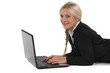 A businesswoman lying on the floor with her laptop.