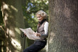 A mature woman resting on a tree, looking at a map, close up