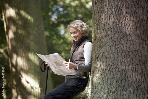 Photo: A mature woman resting on a tree, looking at a map, close up A mature woman resting on a tree, looking at a map, close up