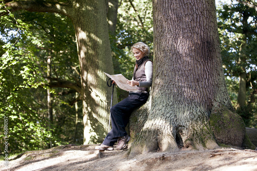 Photo: A mature woman resting on a tree, looking at a map A mature woman resting on a tree, looking at a map