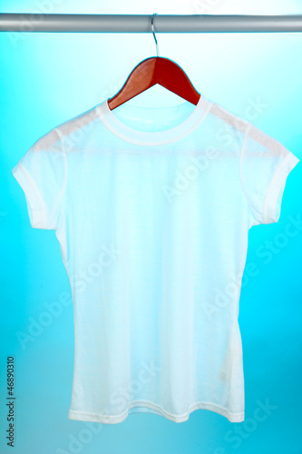 Photo: White t-shirt on hanger on blue background White t-shirt on hanger on blue background