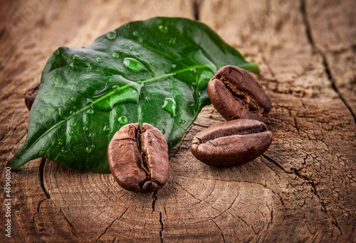 Photo: Coffee grains and green leaf on grunge wooden background Coffee grains and green leaf on grunge wooden background
