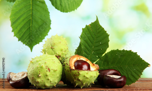 Photo: Chestnuts with leaves on wooden table on green background Chestnuts with leaves on wooden table on green background