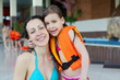 Happy wet mother and little daughter hug after swimming in pool.