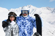 Happy couple in sport suits and helmets stand with snowboard