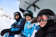 Three happy skiers in helmets and sport suits ride on funicular