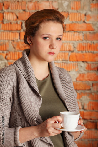 Photo: brown-haired woman hold cup, plate near brick wall, half body brown-haired woman hold cup, plate near brick wall, half body