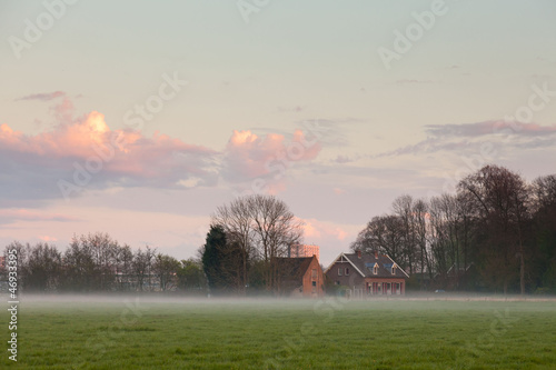 Photo: Meadow with house in the mist at sunset. Cloudy sky. Meadow with house in the mist at sunset. Cloudy sky.