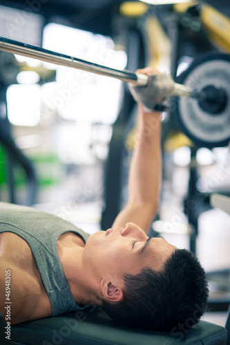 Photo: Young man lifting the barbell in the gym. Young man lifting the barbell in the gym.