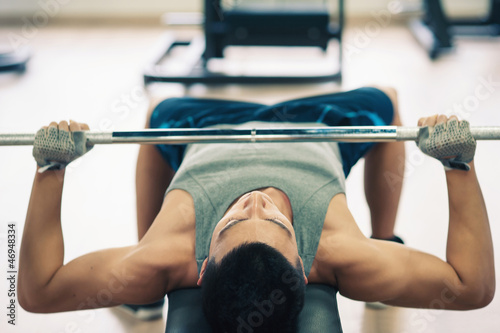 Photo: Young man lifting the barbell in the gym. Young man lifting the barbell in the gym.