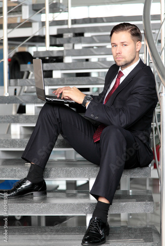 Photo: A businessman sitting on stairs smiling with a laptop computer A businessman sitting on stairs smiling with a laptop computer