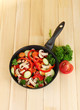 frying pan with vegetables on wooden background