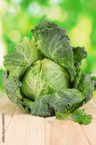 Photo: Fresh savoy cabbage on wooden table on natural background Fresh savoy cabbage on wooden table on natural background